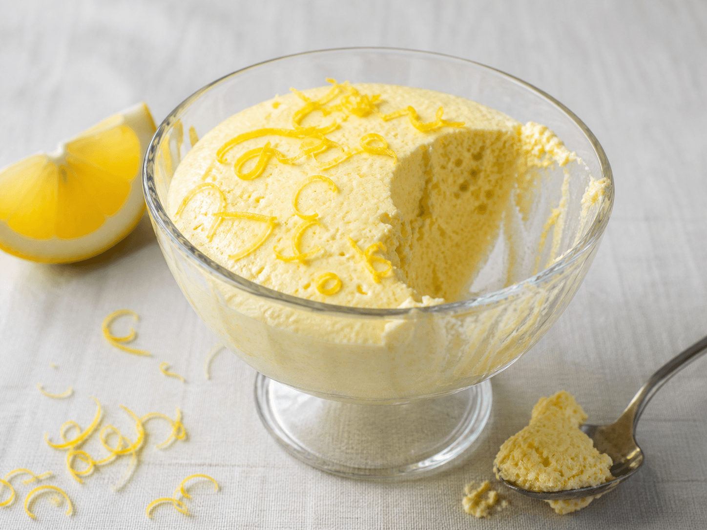 Citronfromage i glasskål med en naturlig skefuld taget fra siden.