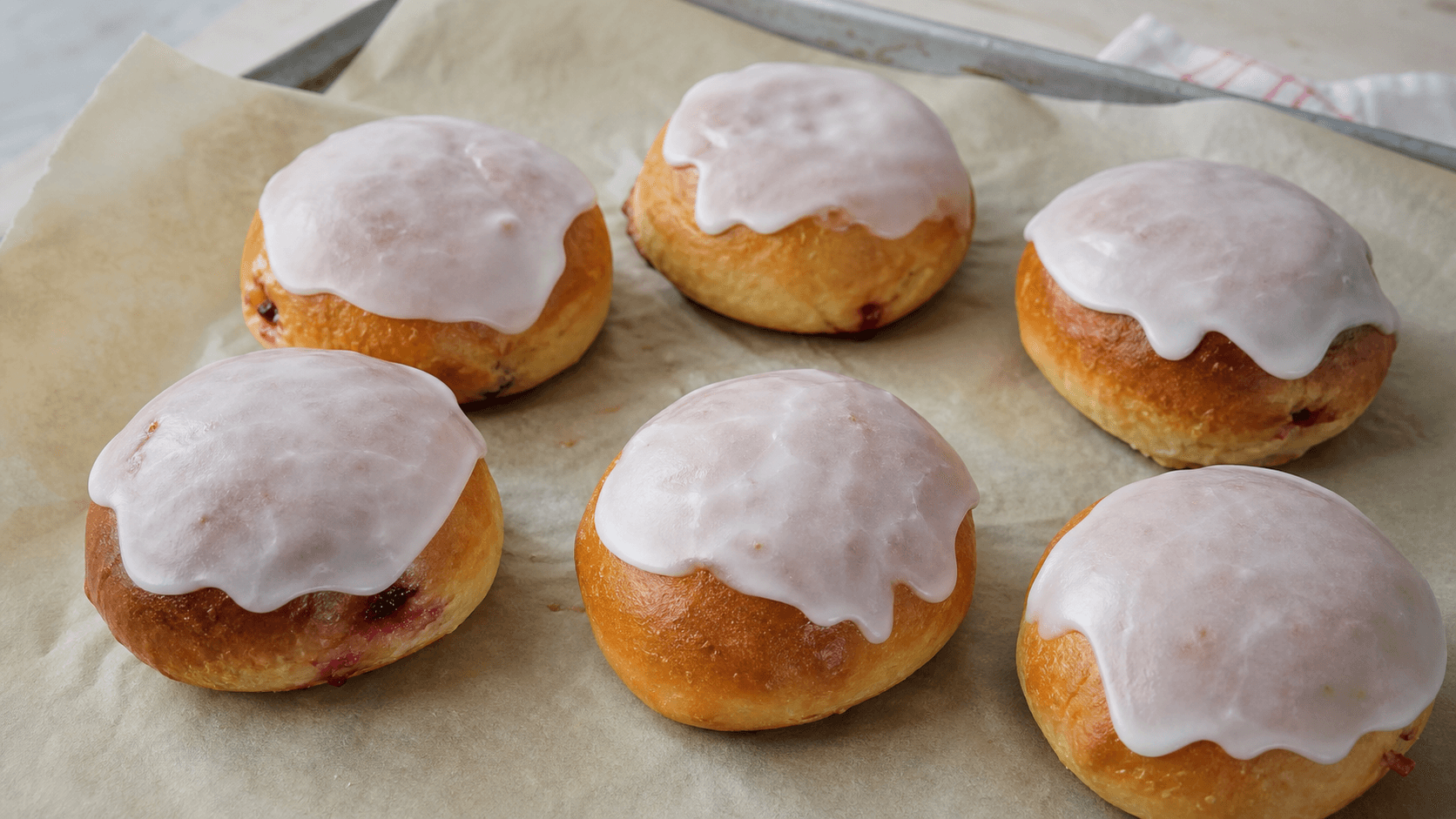 Lukkede fastelavnsboller med hindbær og creme indeni, lyserød glasur og små hindbærspor ved samlingen.