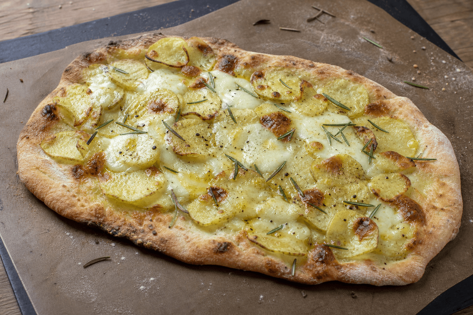 Rustik kartoffelpizza i ujævn frihåndsform med tynde kartoffelskiver, mozzarella og rosmarin.