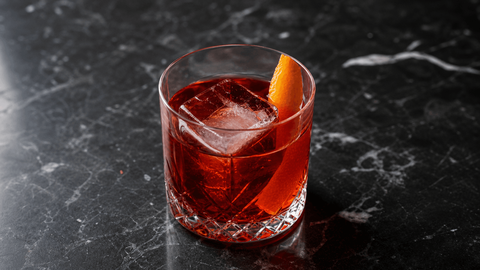 Negroni i lavt glas med stor isterning, rubinrød drink og appelsinskal.