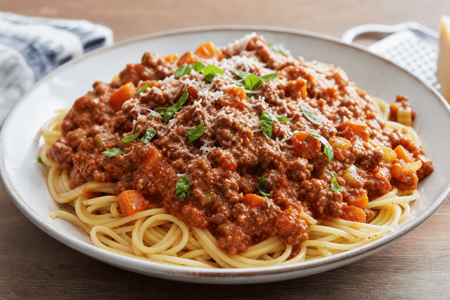 Pasta med kødsovs på tallerken med spaghetti, rødbrun hakkekødssauce, ost og persille.