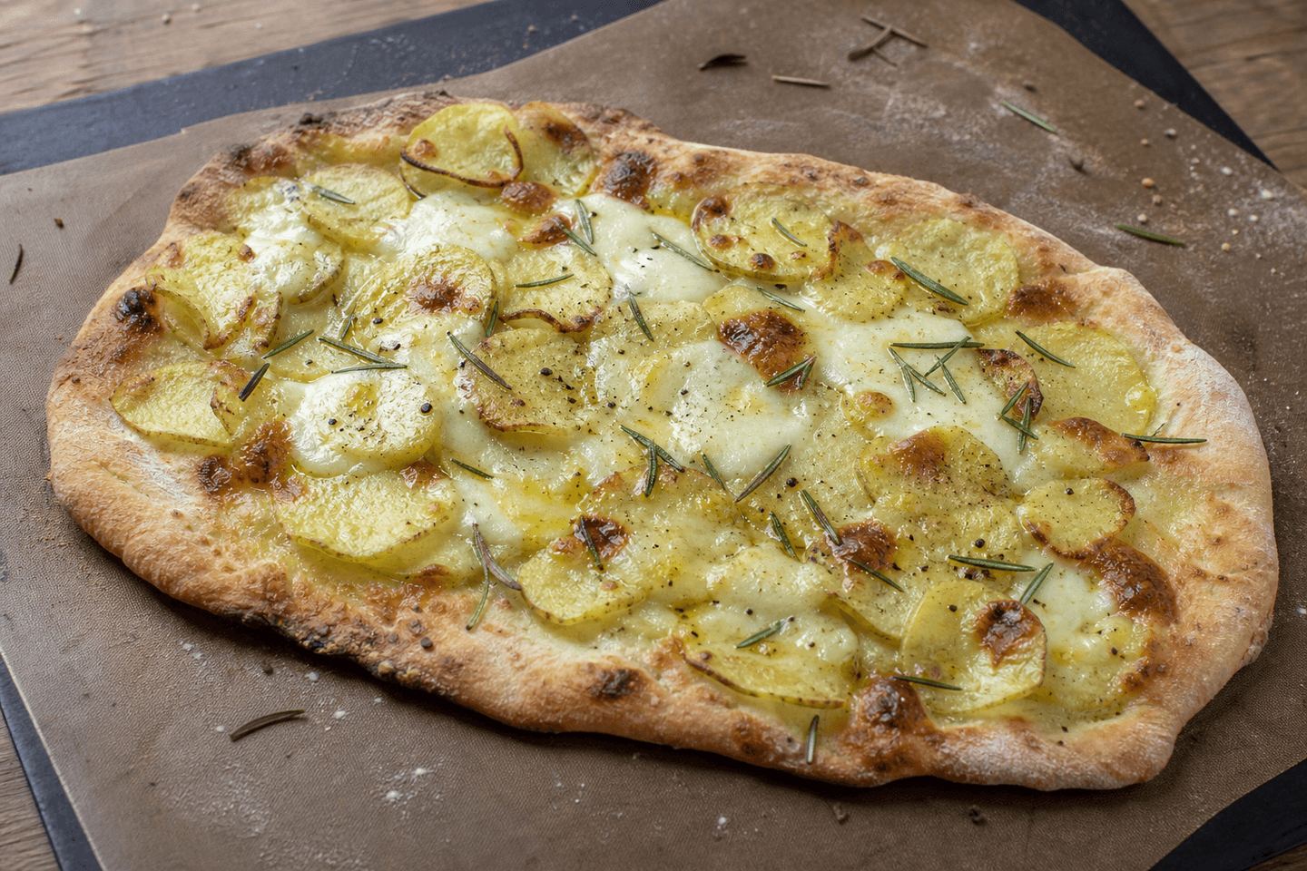 Rustik kartoffelpizza i ujævn frihåndsform med tynde kartoffelskiver, mozzarella og rosmarin.