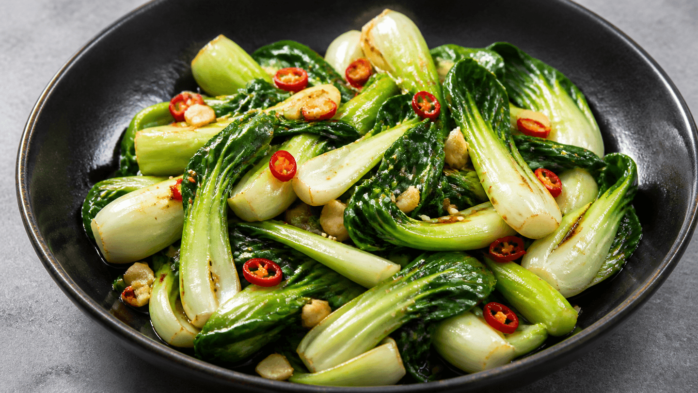 Pak choi wok i mørk skål med blanke grønne blade, hvide stilke, chili og sesam.