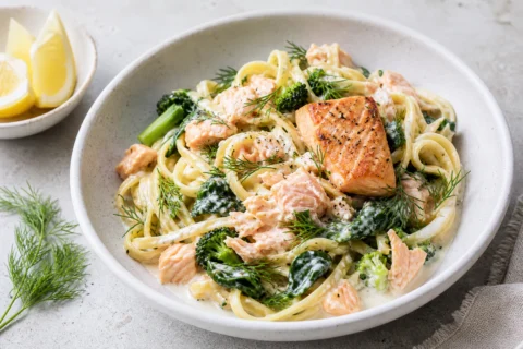 Pasta med laks i lys skål med cremet pasta, laksestykker, spinat, dild og citron.